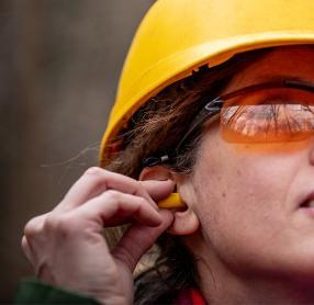 Woman in hard-hat and goggles putting in ear plug