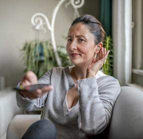 Middle-aged woman with hearing aid struggling to hear television