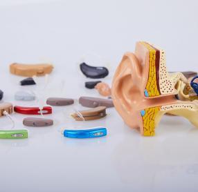 Table covered with hearing aids beside medical model of ear