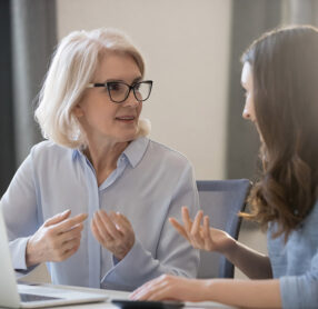 Senior woman talking with younger woman in front of laptop